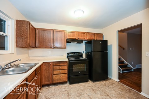 A kitchen with a black refrigerator and wooden cabinets.