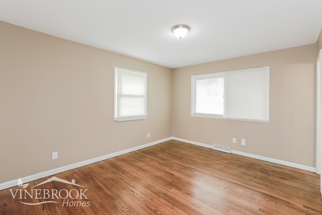 the living room of a home with wood flooring and two windows