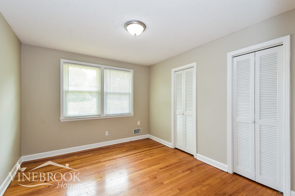 a bedroom with a hardwood floor and two closets and a window