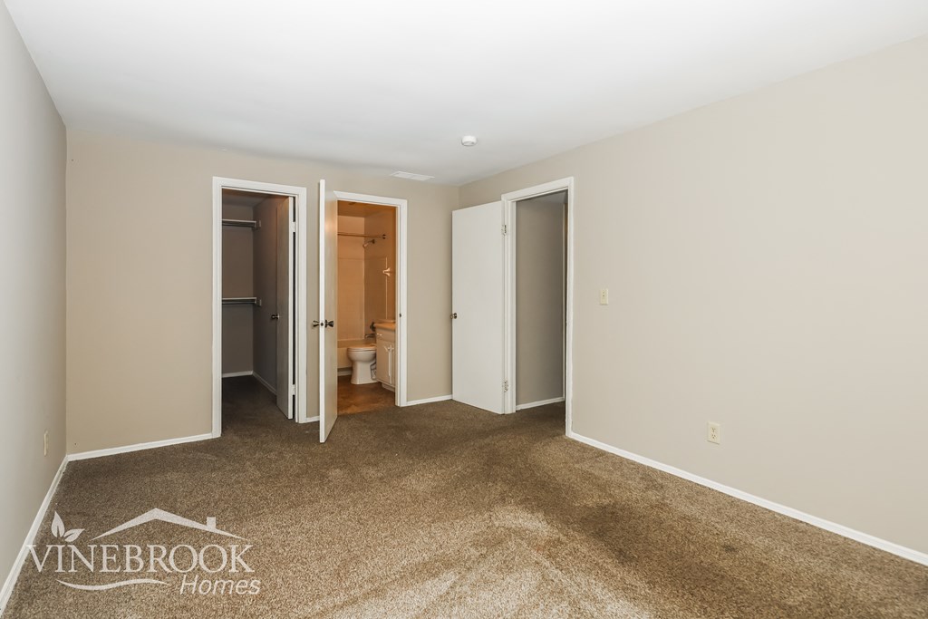a bedroom with a carpeted floor and white walls and doors to a bathroom