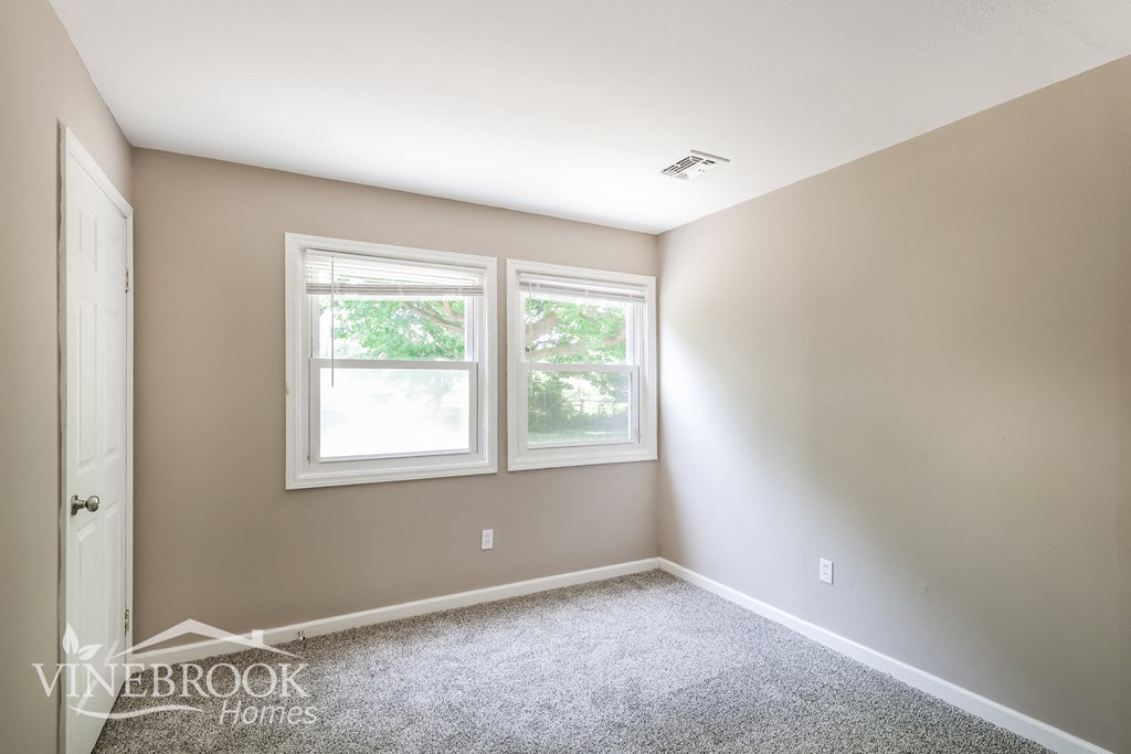 a empty room with two windows and a carpeted floor