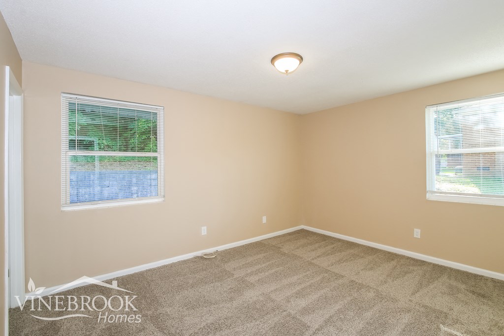 the living room of a house with carpet and two windows
