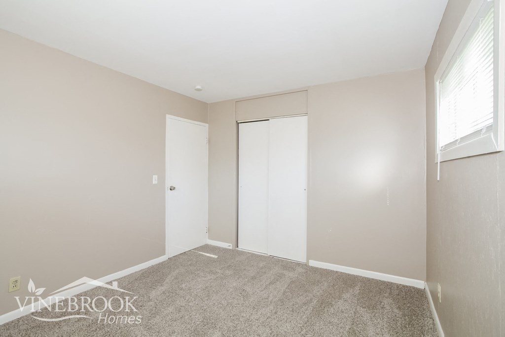 a bedroom with a closet and a window and a carpeted floor