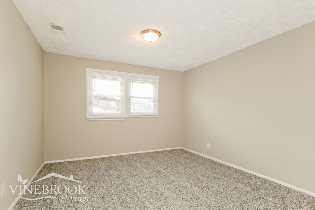 A room with a carpeted floor and a window with blinds.
