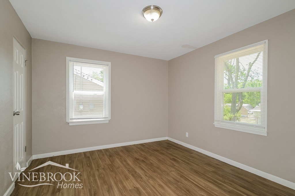 a bedroom with a hardwood floor and two windows