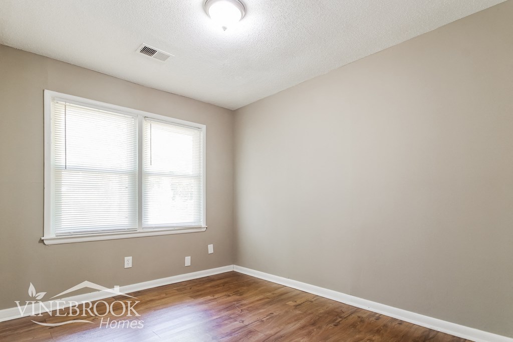 a bedroom with a hard wood floor and two windows