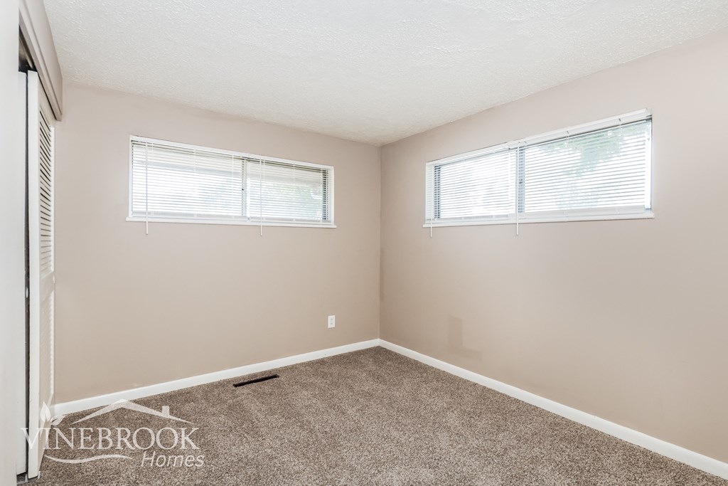 an empty room with carpet and two windows