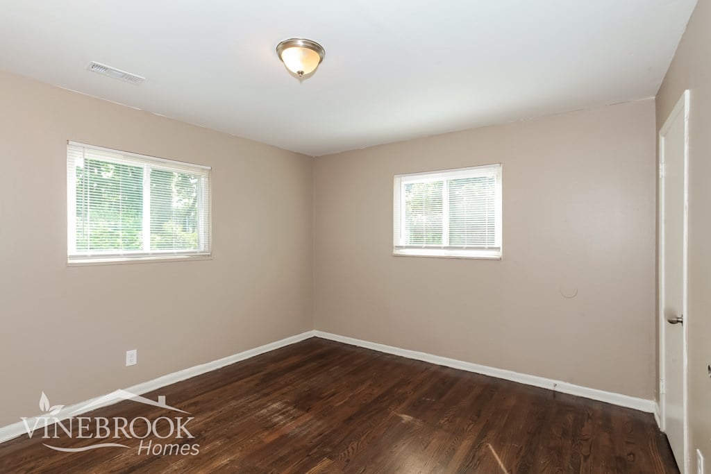 A room with wooden floors and two windows.