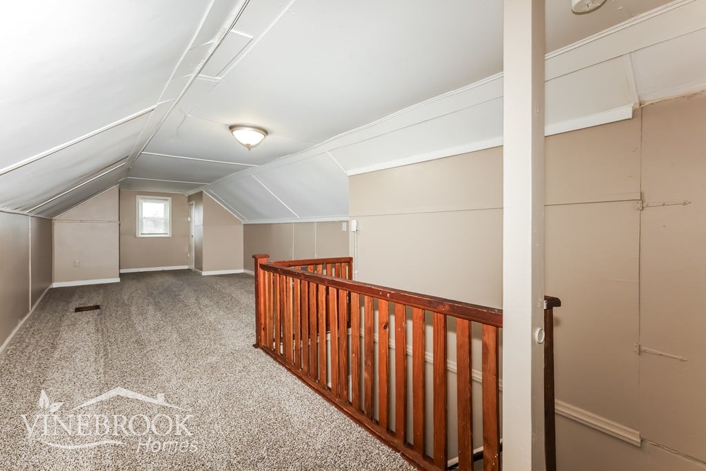 A spacious attic room with a carpeted floor and a wooden railing.