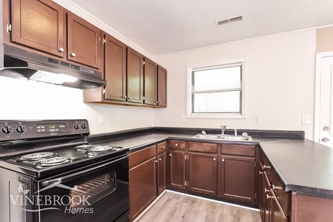 A kitchen with a black stove top oven and brown cabinets.