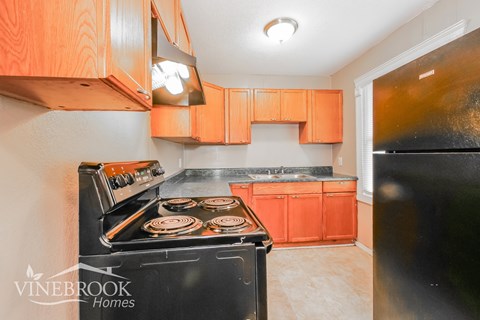A kitchen with a black stove top oven and orange cabinets.