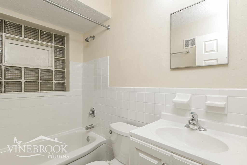 A white bathroom with a tub, sink and mirror.