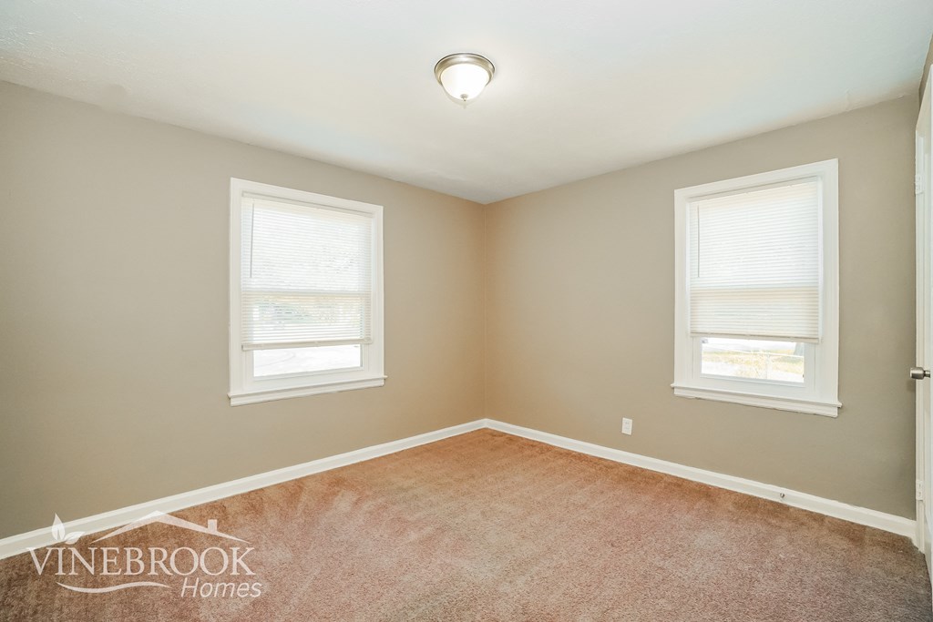 an empty room with two windows and a carpet