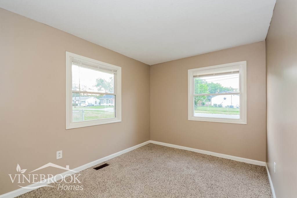 a bedroom with two windows and a carpeted floor