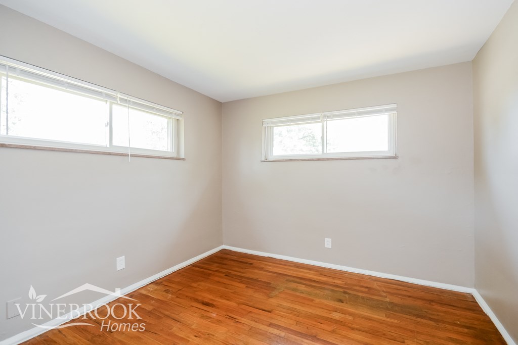 a bedroom with wood flooring and two windows