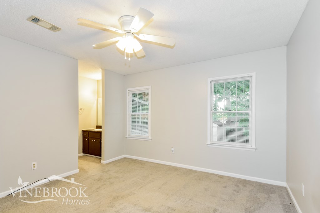 a spacious living room with a ceiling fan and white walls