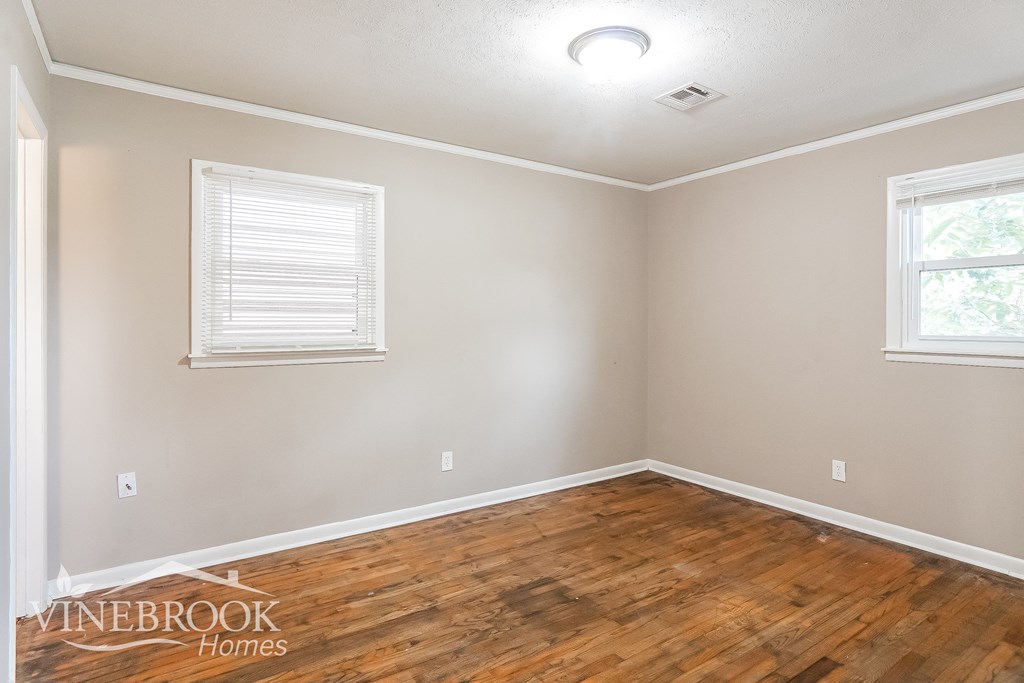 the living room of a house with wood flooring and two windows