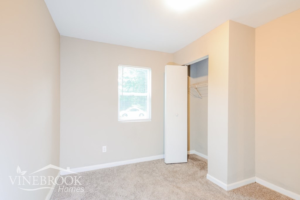 a bedroom with a closet and a window and a carpeted floor
