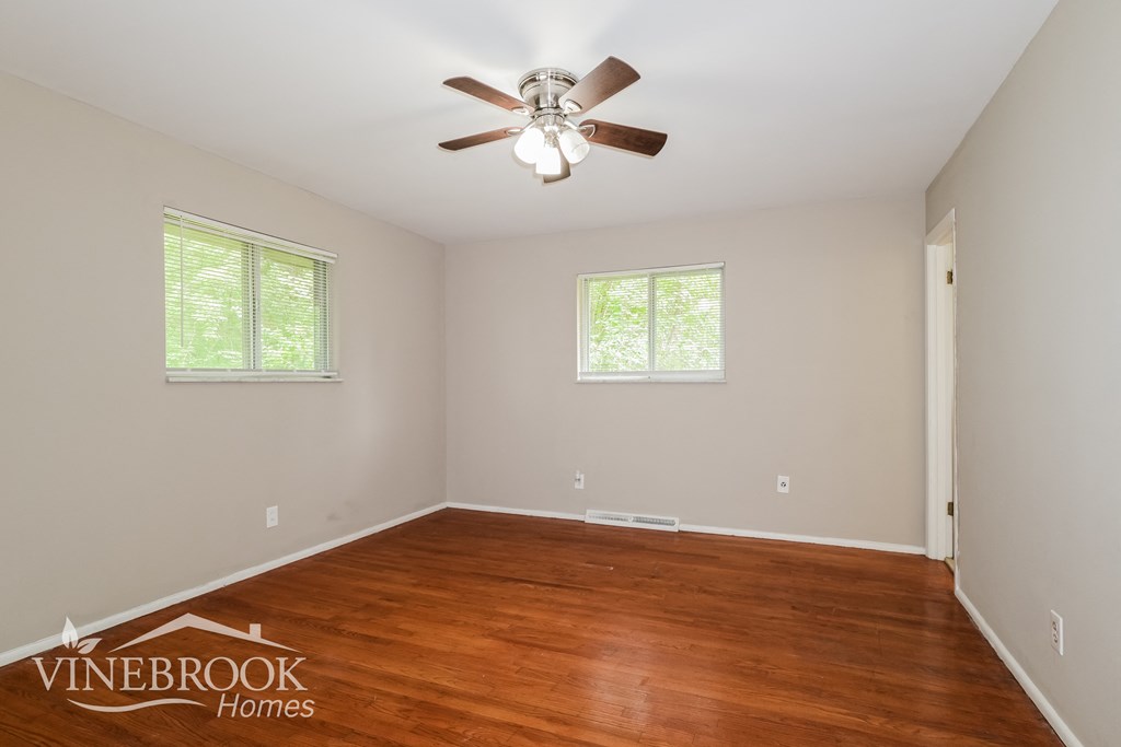 A room with a ceiling fan and two windows.