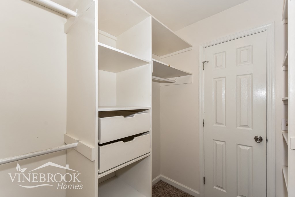 a walk in closet with white shelves and a white door