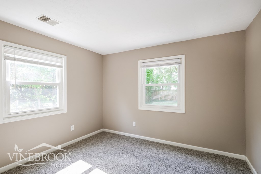 a bedroom with two windows and a carpeted floor