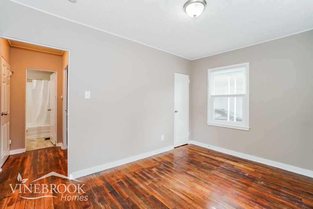 the living room of a home with wood flooring and a door to the bathroom