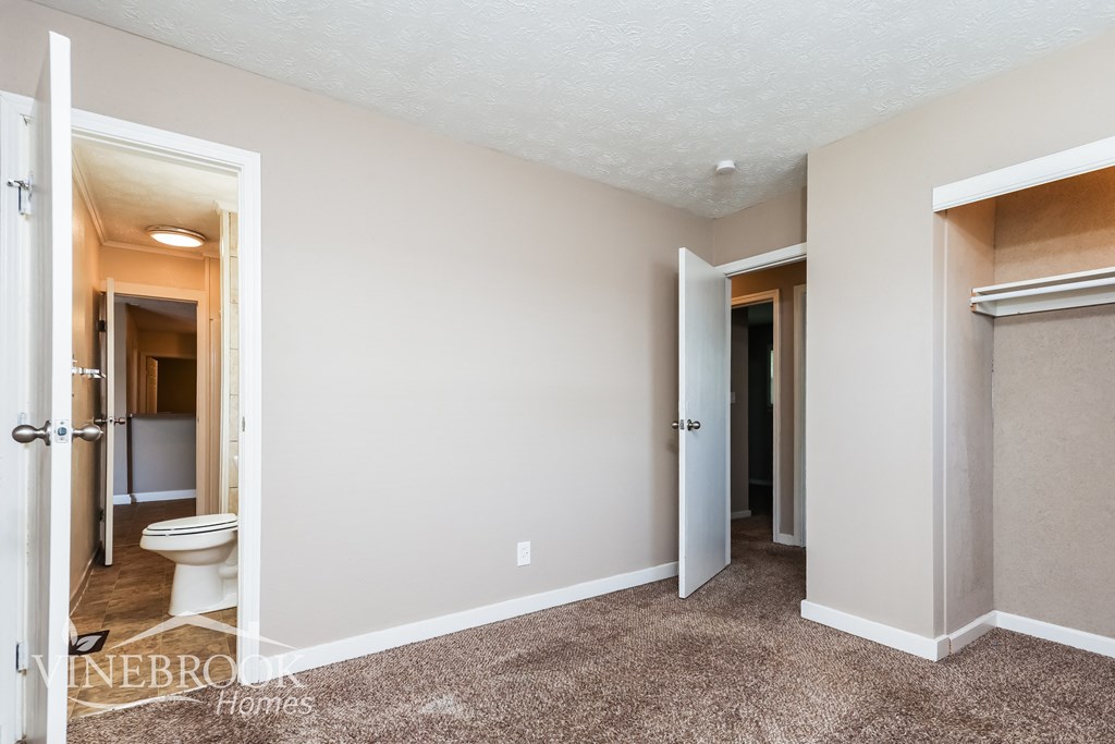 a bathroom with a toilet and a hallway with a door to a closet