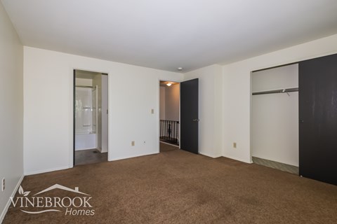 A spacious room with a carpeted floor and white walls, with a door on the right and a mirror on the left.