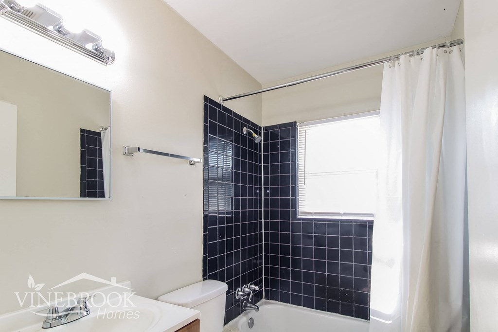 a black tiled bathroom with a tub and a toilet and a sink