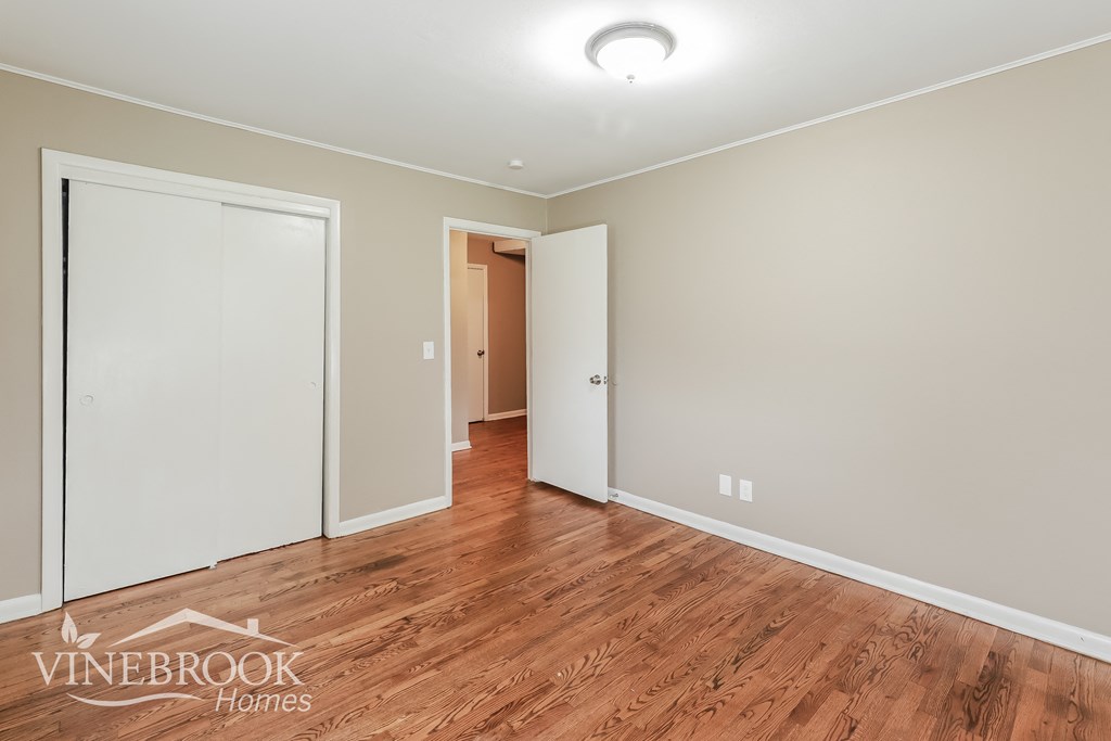 a bedroom with a hardwood floor and white walls and a door to a hallway