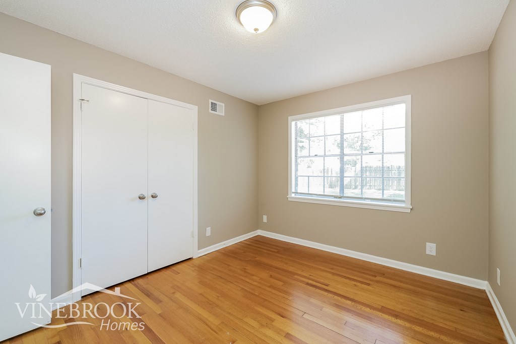 a bedroom with a hardwood floor and white closet and a window