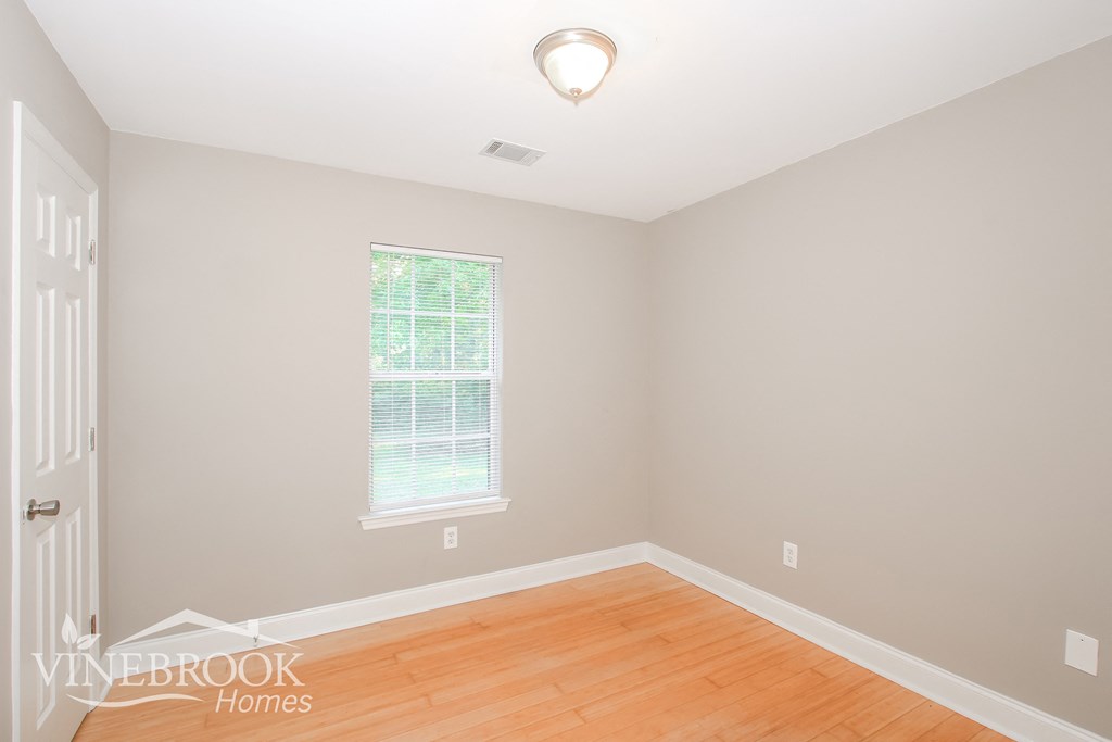 a bedroom with a hardwood floor and white walls and a window