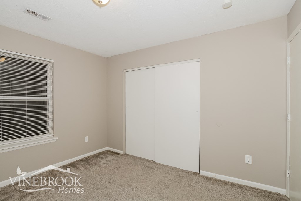 a bedroom with a closet and a window and a carpeted floor