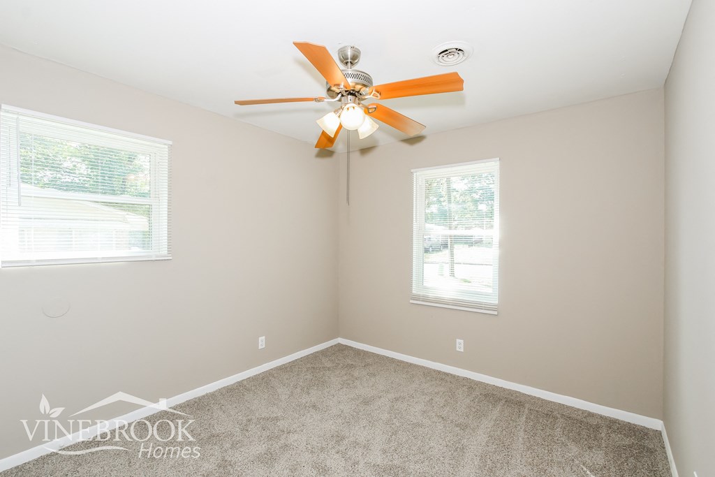 a bedroom with a ceiling fan and two windows