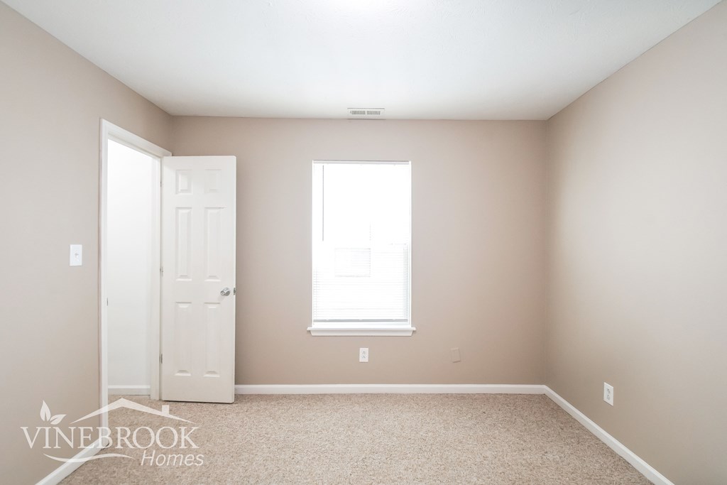 a blank bedroom with a white door and a window