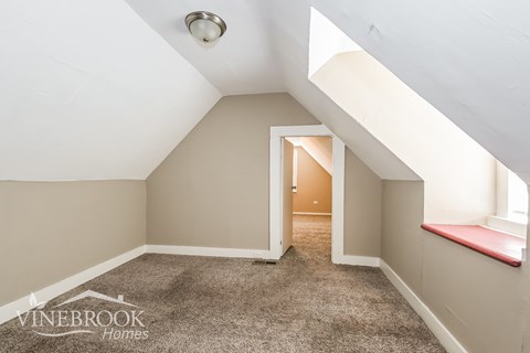 A room with a carpeted floor and a window with a red ledge.