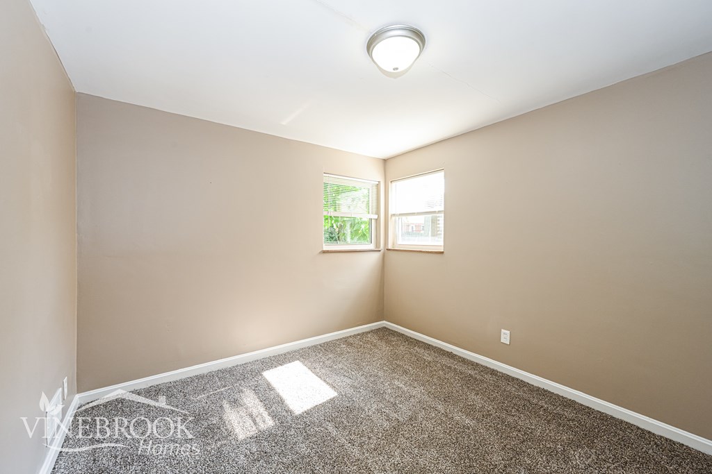 A room with a carpeted floor and a window with a view of trees.