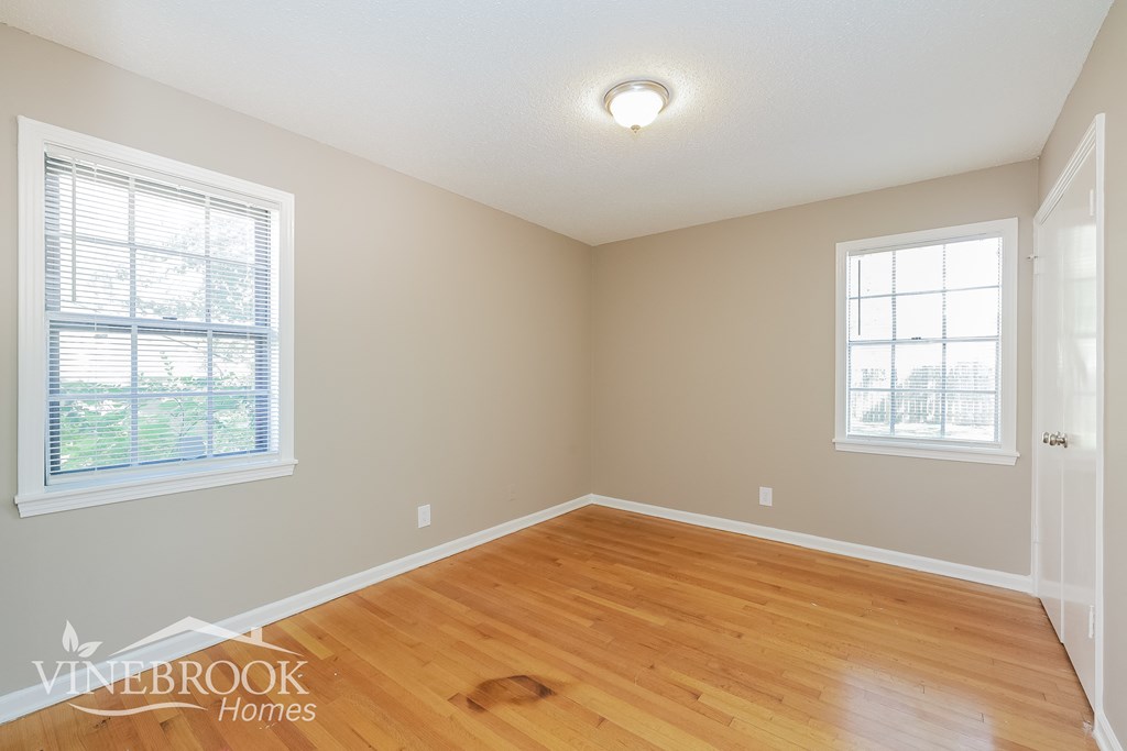 an empty living room with wood floors and two windows