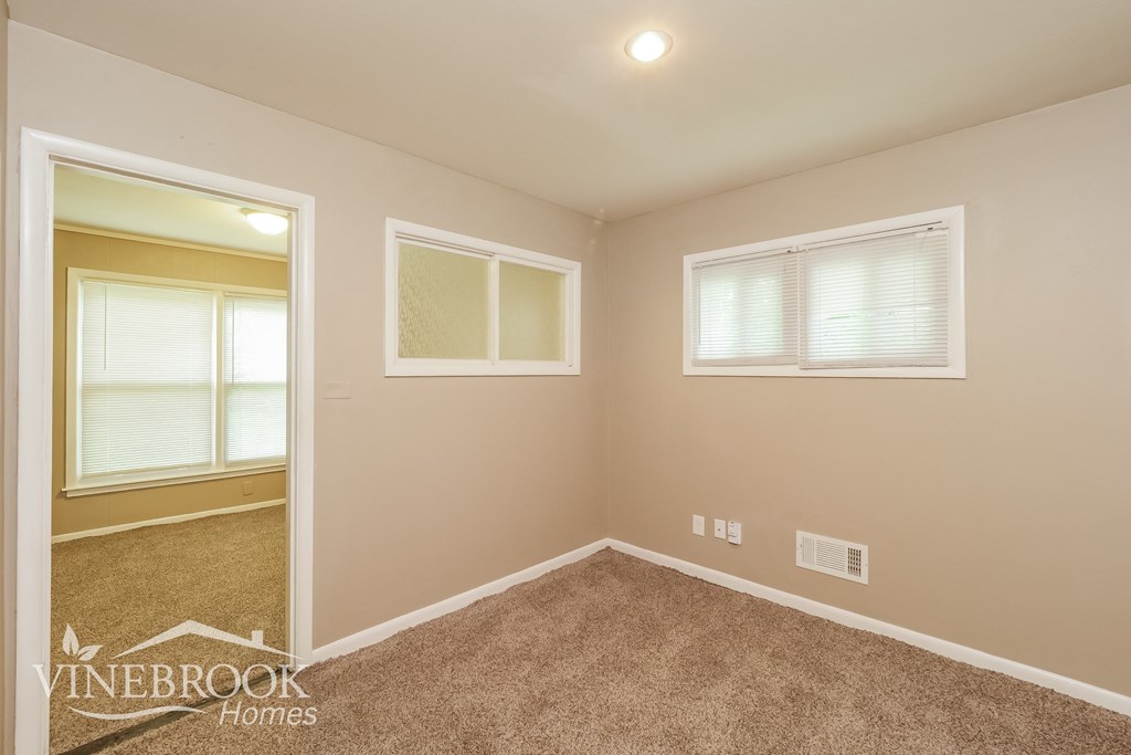 the bedroom of a house with carpet and two windows