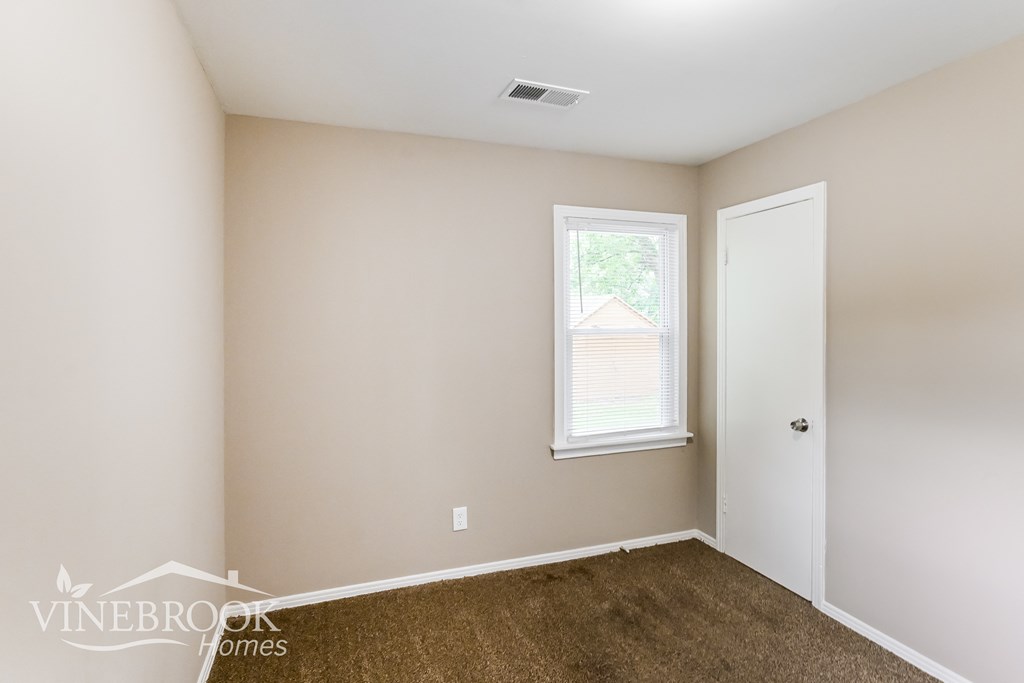 a bedroom with brown carpet and a white door and a window
