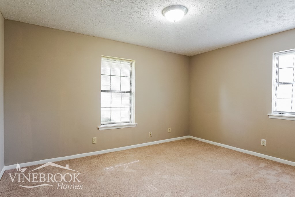 the living room of a home with beige carpet and two windows