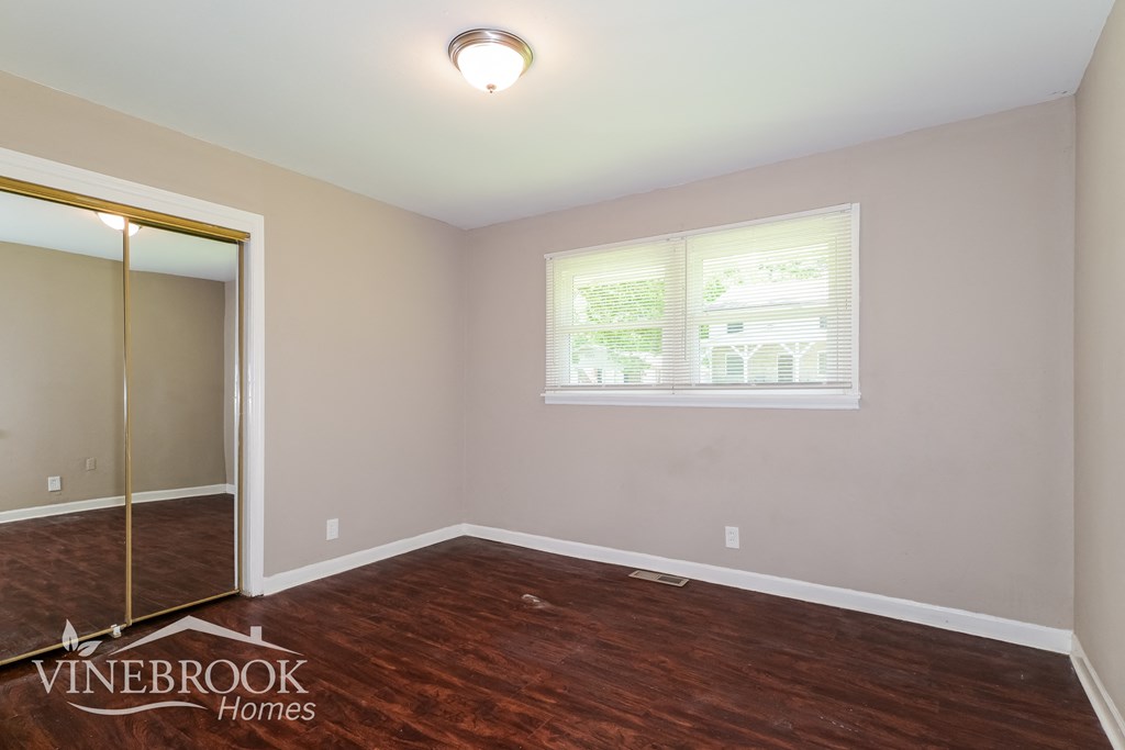 the second bedroom after renovation with wood flooring and a mirrored closet