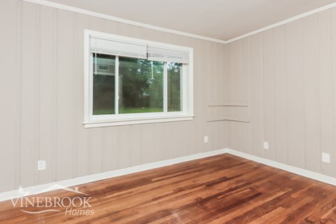 A room with wooden floors and a window showing trees outside.