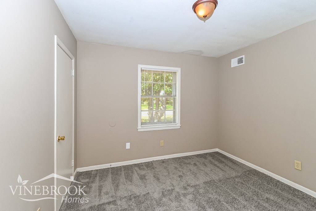 A room with a carpeted floor and a window with a view of trees.