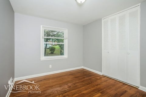 A room with a window showing trees outside and a wooden floor.