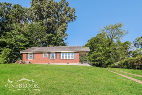 a small brick house on a grassy hill with trees