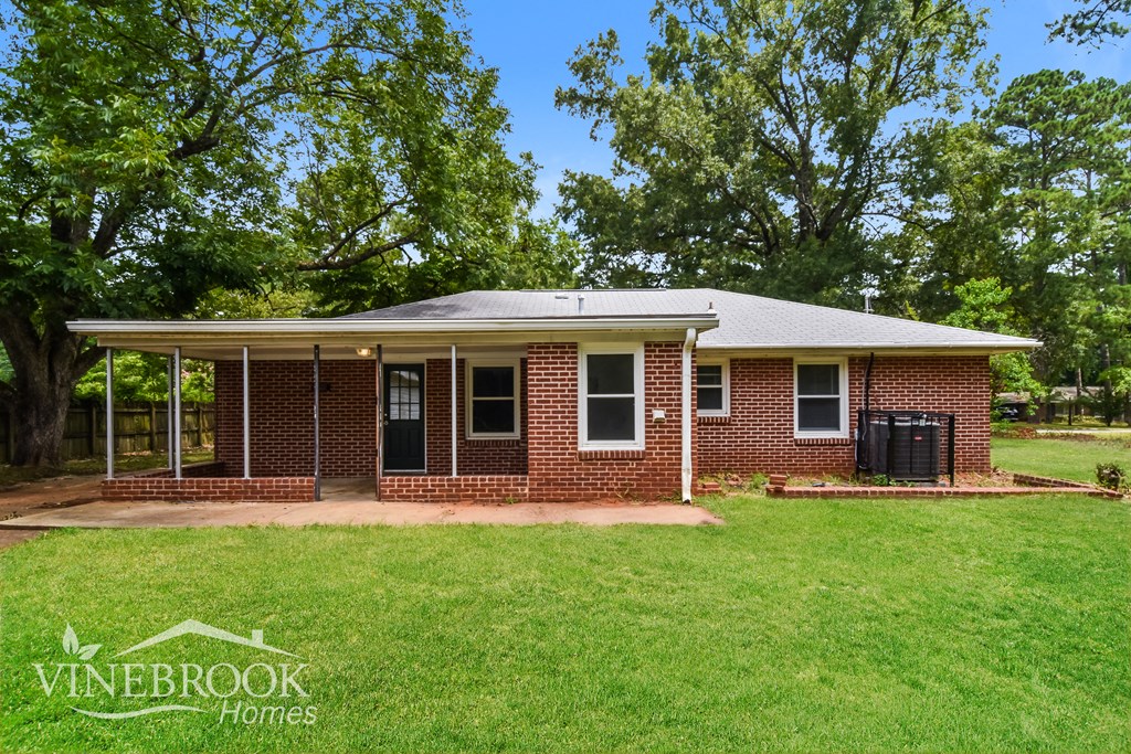 a small brick house with a covered porch and a green lawn