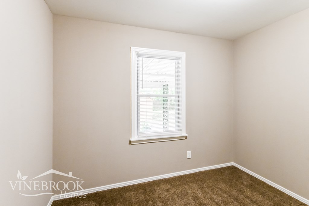 a bedroom with a window and a brown carpet