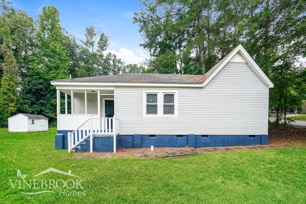 A small house with a porch and a small shed in the background.