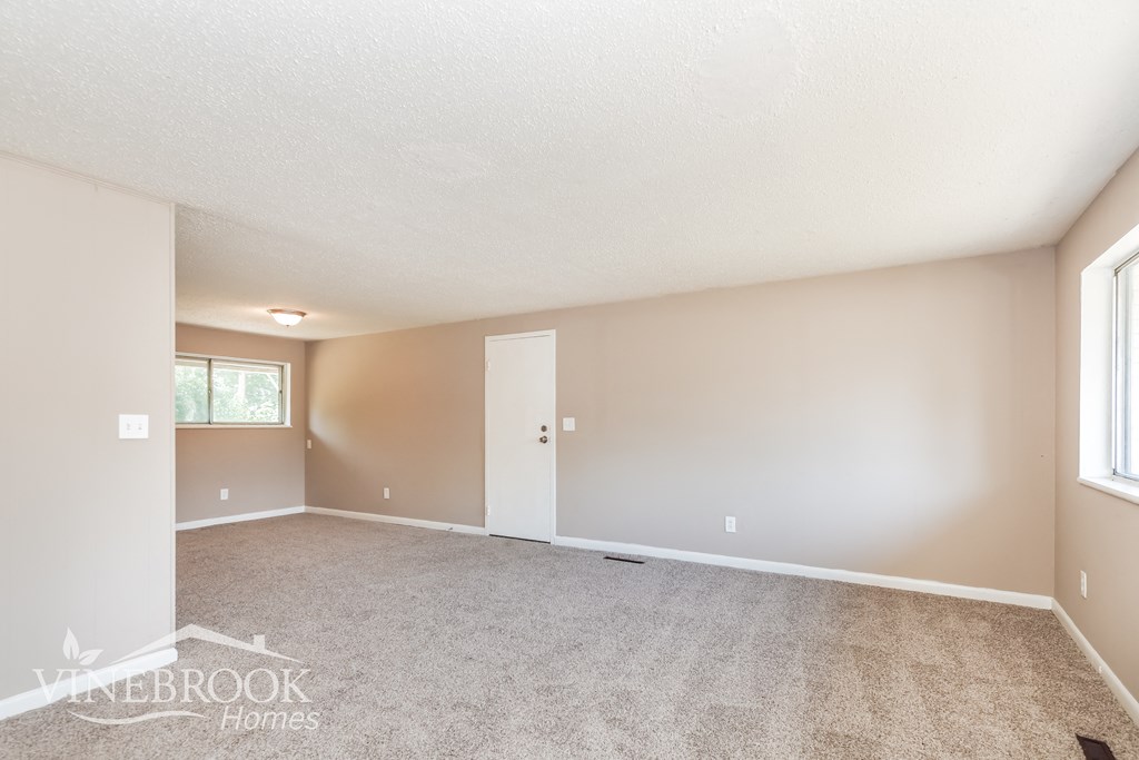 a spacious living room with carpet and a door to a bedroom